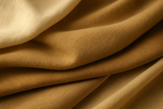 Close-up of layered natural fabrics — raw silk, soft cashmere, virgin wool, and breathable linen — captured in warm daylight highlighting texture and drape.