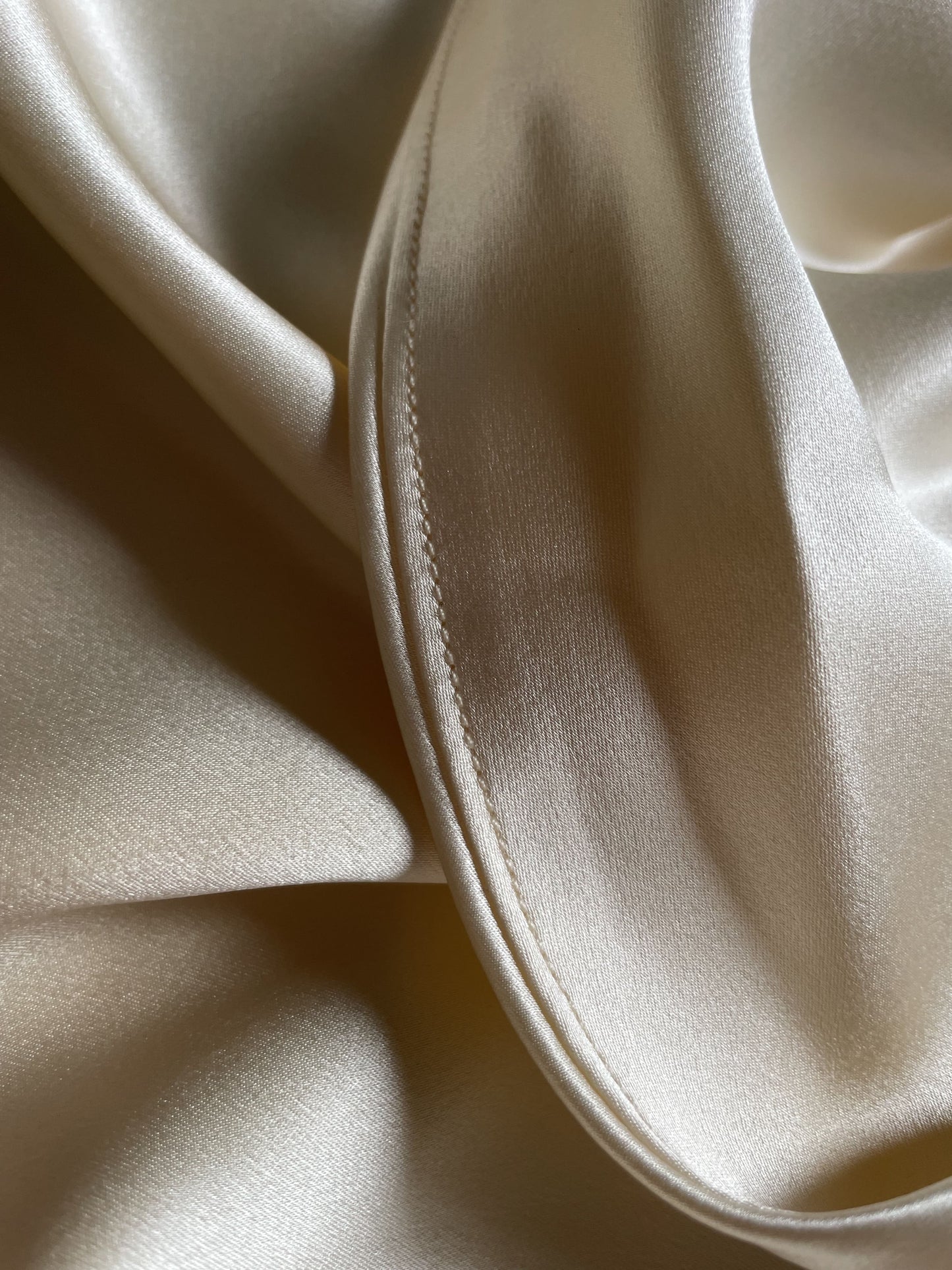 Close-up of champagne bias cut silk slip dress hem.