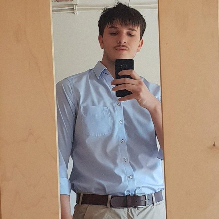 Bradic founder taking a mirror selfie wearing a light blue shirt and beige pants.