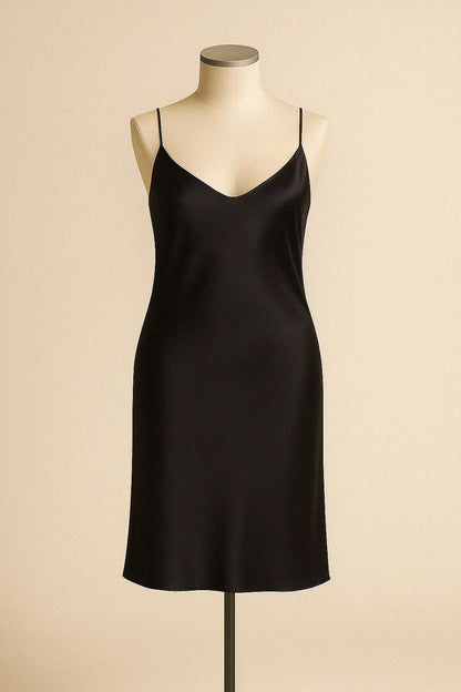 Black bias cut silk slip dress on a mannequin against a beige background