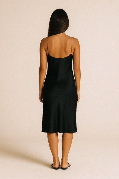Back of a woman wearing a black bias cut silk slip dress against a beige background