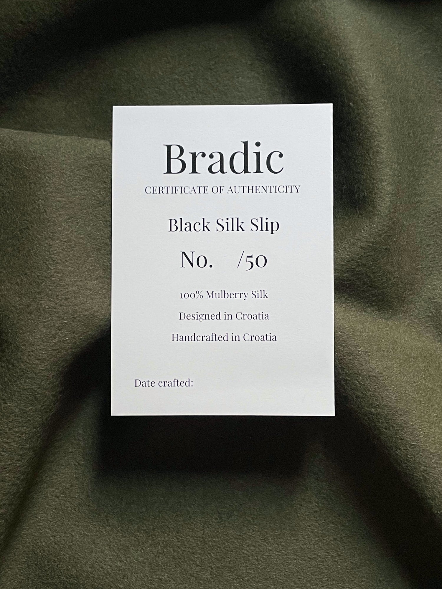 Bradic certificate of authenticity for a black silk slip on a textured green fabric background