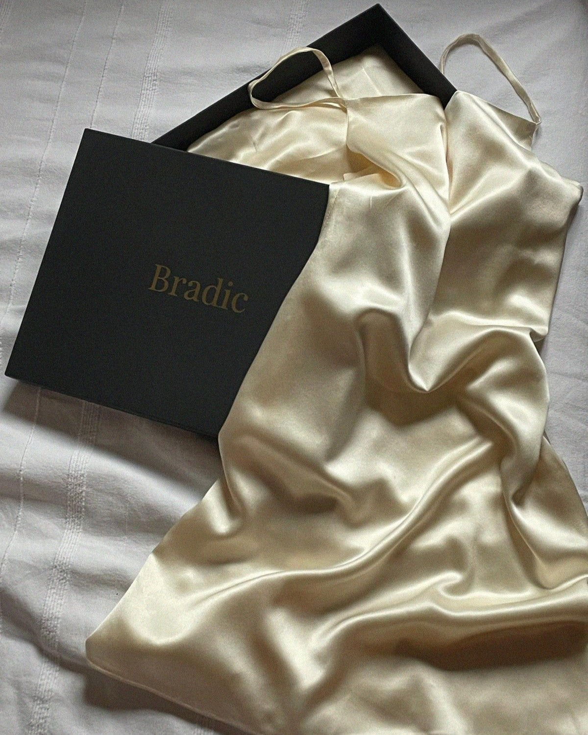 Straight cut champagne silk slip dress laying flat across Bradic packaging.