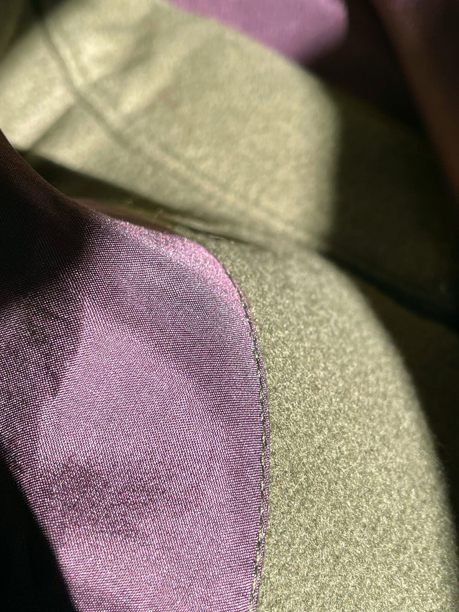 Close up seam of olive wool vest with burgundy silk lining.